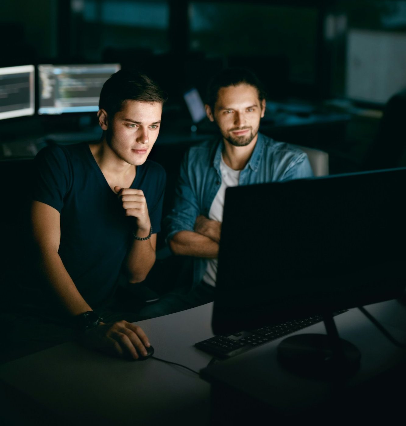 Dos ingenieros revisando la actividad de agentes en un monitor de noche